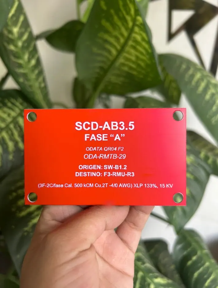 Placa roja de identificación eléctrica con fase, origen y destino grabados en blanco