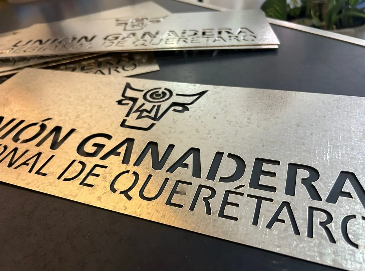 Placas de lámina galvanizada con un logotipo y texto calados, apiladas sobre una mesa